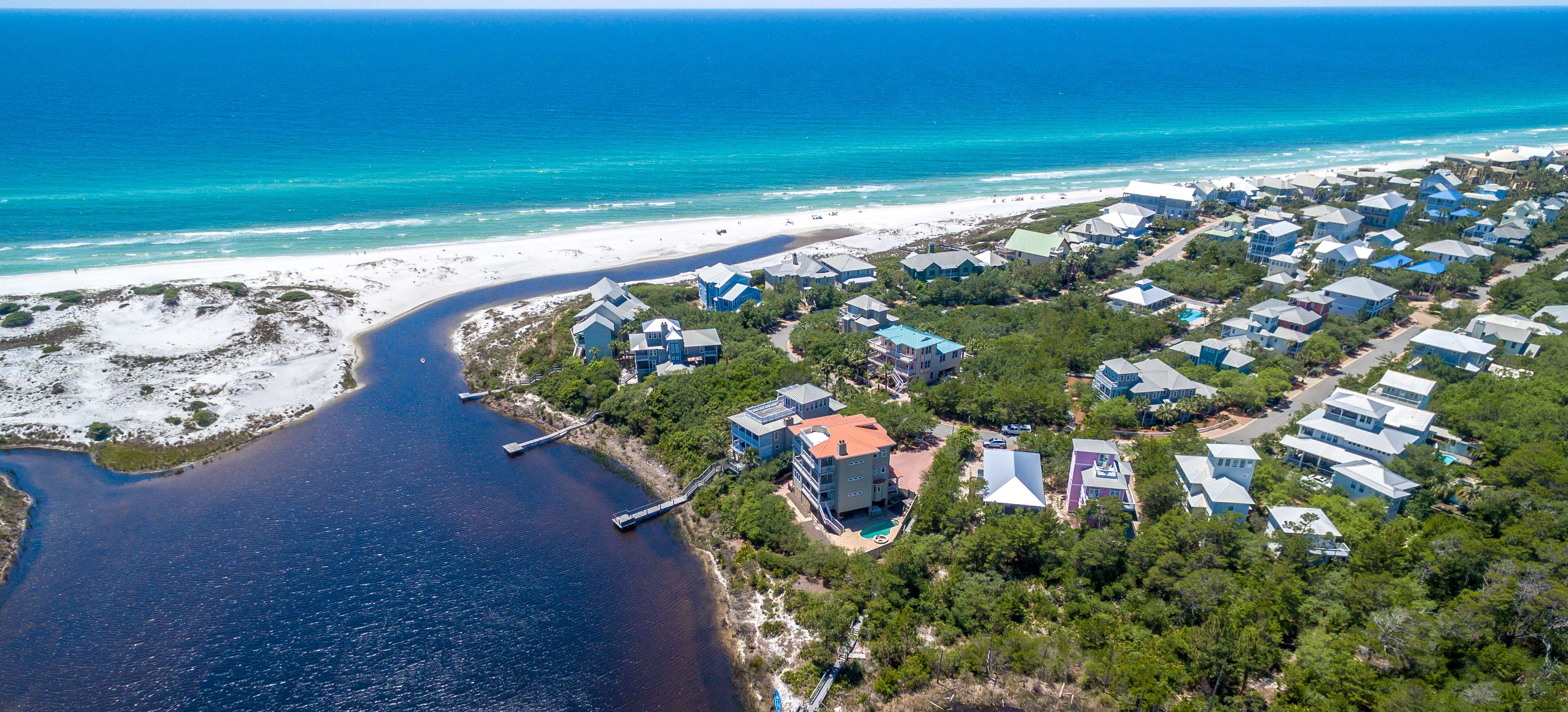 An aerial view of homes in Old Florida Beach surrounding Eastern Lake and its outfall onto the beach with the brilliant blue gulf in the background